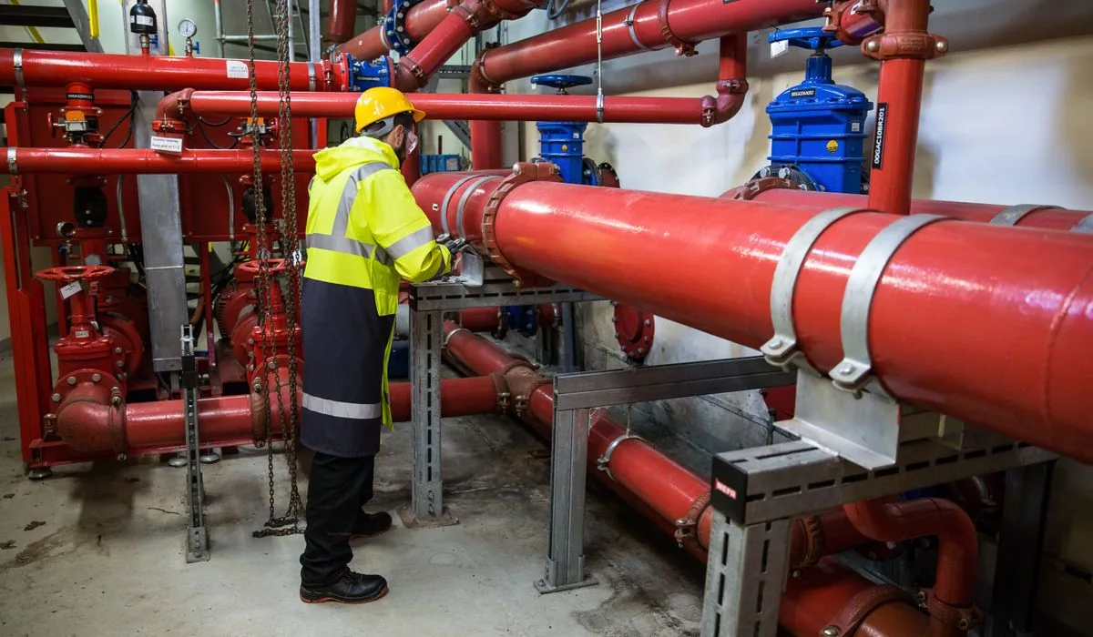 A technician inspecting valves on large red water supply pipes in a mechanical room