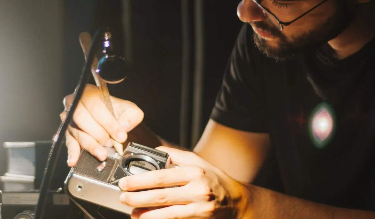 A camera technician working on a film camera under a bench magnifier