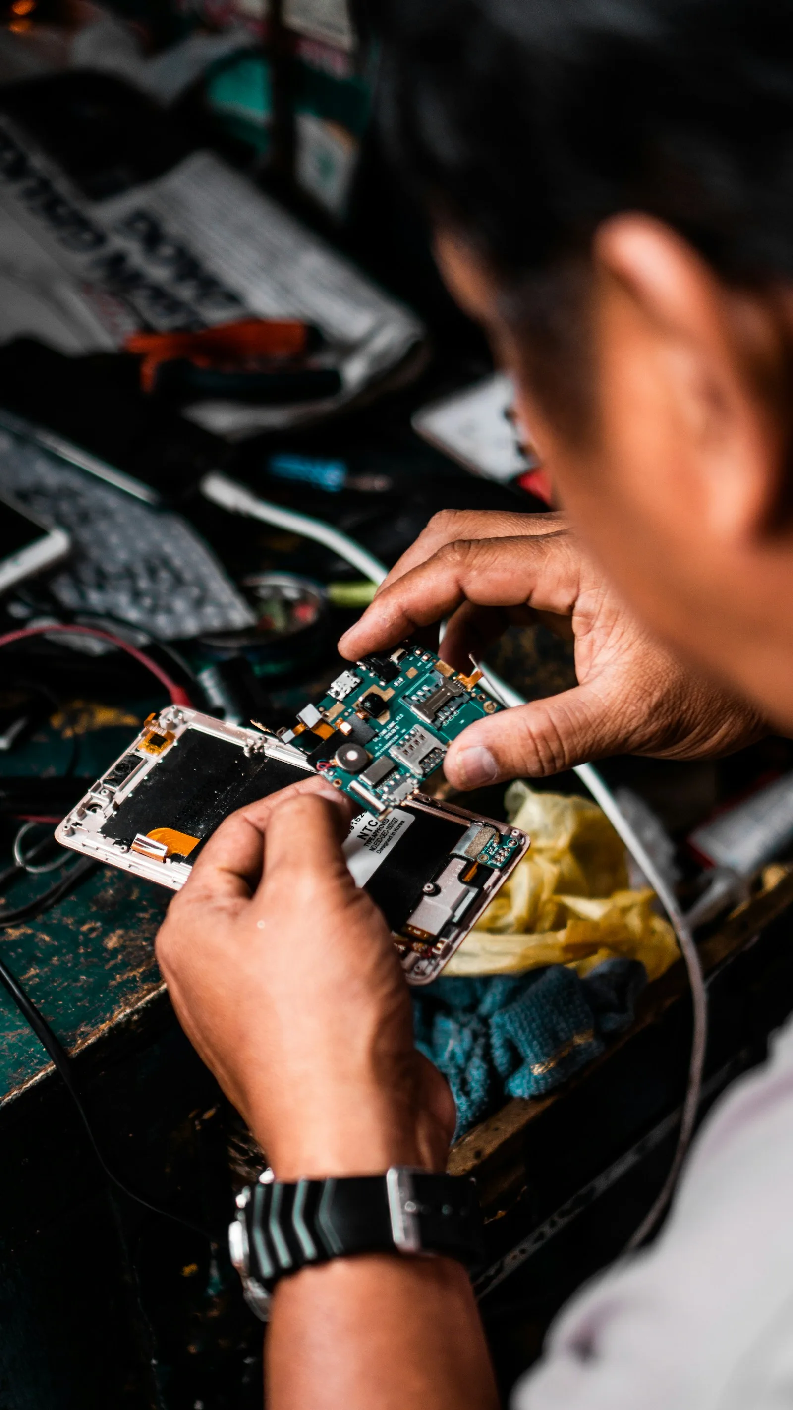 Disassembled iPhone with battery removed, repair tools and components laid out on a wooden workbench, illustrating a typical phone repair job